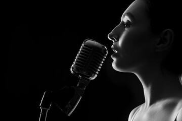 Canvas Print - Silhouette of female singer with microphone on dark background, closeup