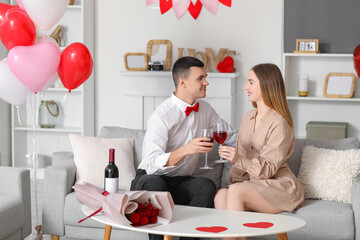 Poster - Beautiful young couple with heart-shaped balloons, bouquet of flowers and wine glasses celebrating Valentine's Day at home