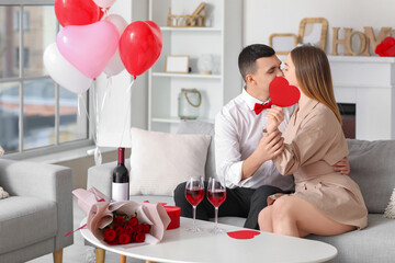 Sticker - Beautiful young couple with paper heart, bouquet of flowers and wine glasses celebrating Valentine's Day at home