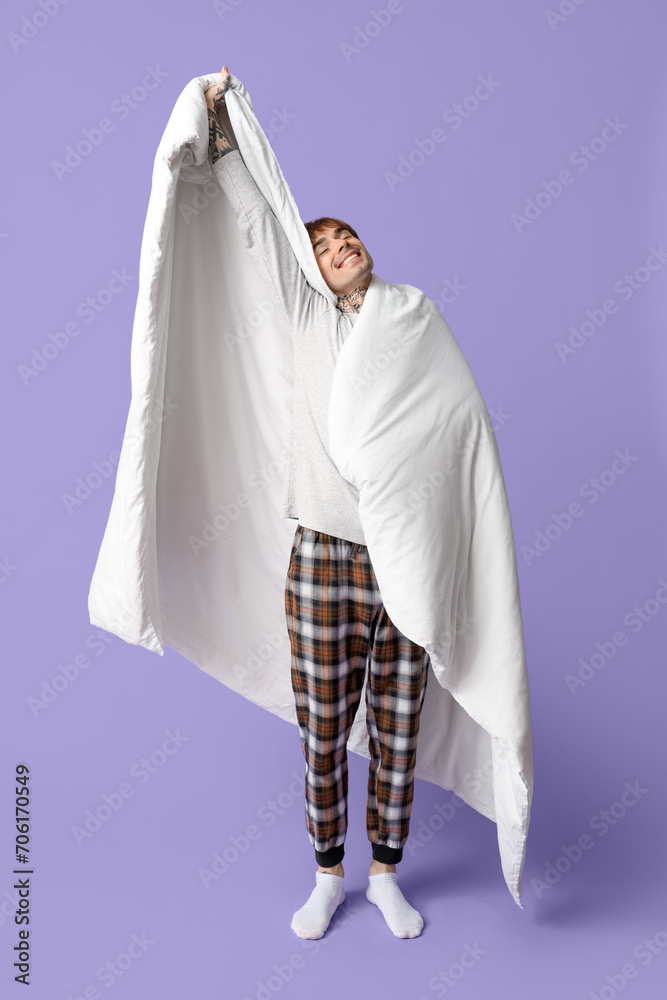 Handsome young man with blanket stretching on lilac background