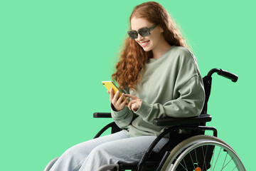 Sticker - Young redhead woman in wheelchair using mobile phone on green background