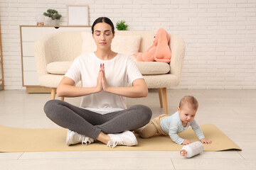 Wall Mural - Beautiful young sporty woman with her little baby meditating at home