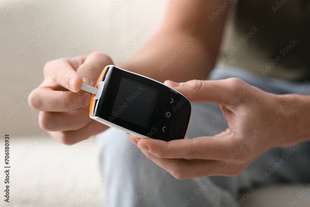 Diabetic young man using glucometer at home, closeup