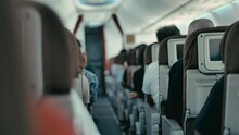 Passengers sit quietly on seats in the cabin of an airplane that is flying