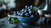 a bowl of blueberries sitting on a table next to a plate of blueberries and a vase of flowers.