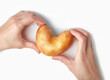 Hands holding heart-shaped potato above white background. Ugly food, funny vegetable, St. Valentine's Day concept. Horizontal orientation, top shot