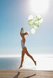 © fStop - Profile of a woman jumping mid air holding a bundle of green balloons