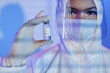 Close up shot of glass medical ampoule vial with COVID-19 vaccine in gloved hand of unrecognizable laboratory scientist dressed in hazmat suit