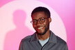 Medium close up shot of smiling bearded Black man in glasses standing at rich pink background and looking at camera
