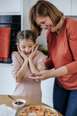 Caucasian woman 60 years old with a girl 8 years old spread jam on cookies in a bright kitchen. The girl shows emotions