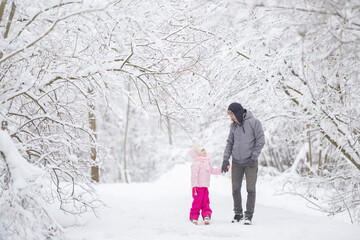 Wall Mural - Smiling father and daughter walking on white fresh snow covered road through tree branches at park after blizzard. Spending time together in beautiful winter day. Enjoying nature stroll. Front view.