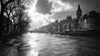 © Kostya - A black and white photograph of a city river with old town architecture and a tower in the background, captured as the sun's rays break through the clouds.