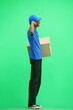 A male deliveryman, on a green background, in full height, with a box, shows strength