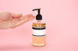 Hand and dispenser for lotion, bath foam or soap isolated on a pink background.