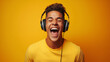 Young man in yellow t-shirt and white headphones, lost in the joy of music. His eyes are closed, and his head thrown back in laughter, against a vivid yellow background, embodying moment of pure bliss