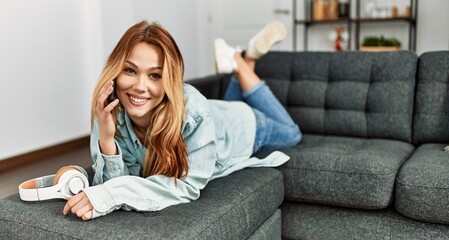 Wall Mural - Young caucasian woman talking on the smartphone lying on sofa at home