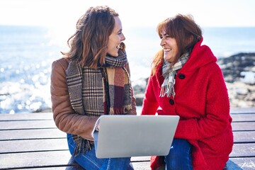 Poster - Two women mother and daughter using laptop sitting on bench at seaside