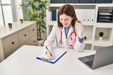 Wall Mural - Young blonde woman doctor writing medical report holding empty test tube at clinic