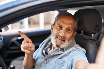 Wall Mural - Cheerful senior man happily pointing to a car while making a joyful selfie outdoors in the city