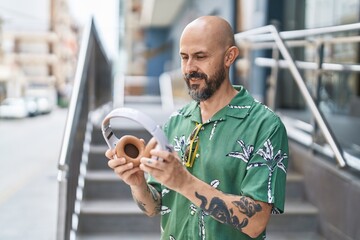 Wall Mural - Young bald man smiling confident holding headphones at street