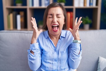 Poster - Middle age hispanic woman sitting on the sofa at home celebrating mad and crazy for success with arms raised and closed eyes screaming excited. winner concept