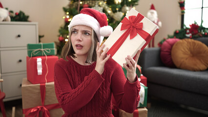 Poster - Young blonde woman hearing gift sound sitting on floor by christmas tree at home