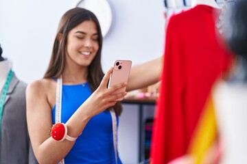 Canvas Print - Young beautiful hispanic woman tailor make photo by smartphone to t shirt at tailor shop