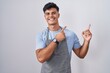 © Krakenimages.com - Hispanic young man wearing apron over white background smiling and looking at the camera pointing with two hands and fingers to the side.