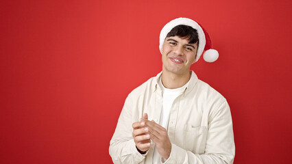 Poster - Young hispanic man wearing christmas hat clapping hands applause over isolated red background