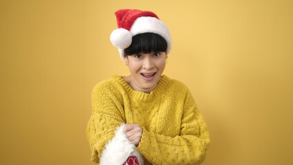 Young chinese woman smiling confident holding christmas sock over isolated yellow background