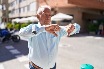 Wall Mural - Middle age grey-haired man doing negative sign with thumbs down at street