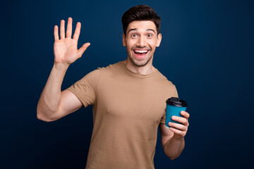 Canvas Print - Photo of friendly cheerful man with bristle dressed beige t-shirt hold capuccino waving palm say hi isolated on dark blue color background