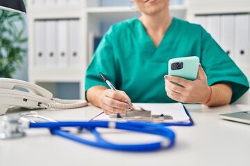 Canvas Print - Young beautiful hispanic woman doctor using smartphone writing on document at clinic