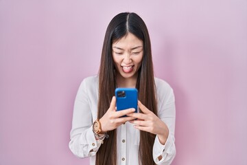 Sticker - Chinese young woman using smartphone typing message sticking tongue out happy with funny expression.