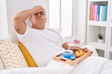 Canvas Print - Young hispanic man eating breakfast in the bed stressed and frustrated with hand on head, surprised and angry face