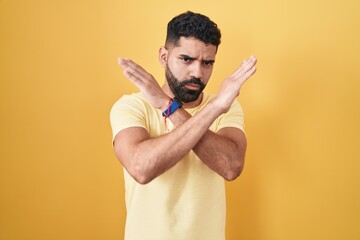 Sticker - Hispanic man with beard standing over yellow background rejection expression crossing arms doing negative sign, angry face