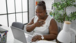 Smiling african american woman confidently working online in the office, equipped with her laptop, hand on chest, embodying success in business