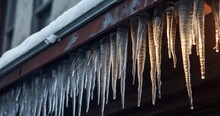 Spiked Icicles At The Edge Of Pitched Gray Roof With Clumps Of Snow In Winter