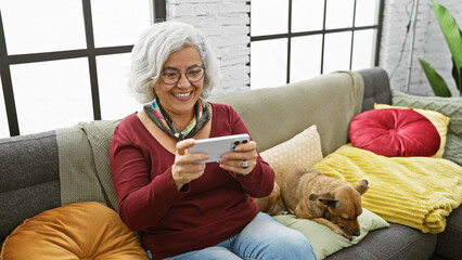 Poster - Smiling grey-haired woman glasses smartphone dog couch cushions livingroom