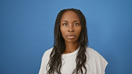 Sticker - Serene african american woman with curly hair posing against a plain blue background for a contemporary portrait.