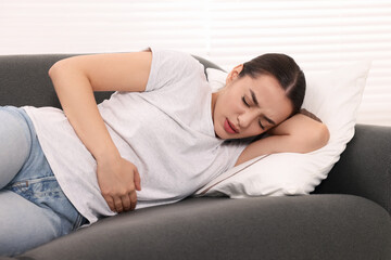 Canvas Print - Woman suffering from abdominal pain while lying on sofa indoors. Unhealthy stomach