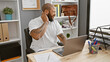 African american man with beard feeling neck pain at office workstation with laptop and decorative plant in background