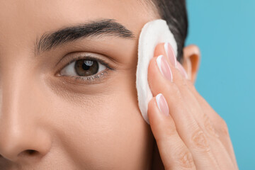 Canvas Print - Beautiful woman removing makeup with cotton pad on light blue background, closeup