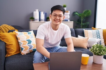 Sticker - Young asian man using laptop at home sitting on the sofa with a happy and cool smile on face. lucky person.