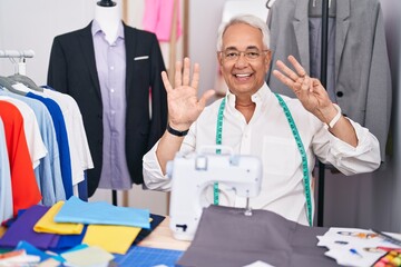 Poster - Middle age man with grey hair dressmaker using sewing machine showing and pointing up with fingers number eight while smiling confident and happy.