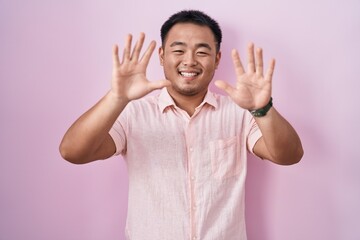 Poster - Chinese young man standing over pink background showing and pointing up with fingers number ten while smiling confident and happy.