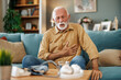 Senior man sitting on sofa at home with sickness