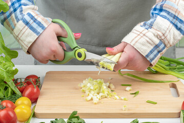 Female hands with kitchen scissors cut green onions.