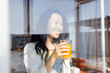 An attractive young Asian woman holds a glass of orange juice and laughs. Reflection in the window.