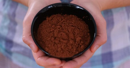 Wall Mural - A woman holding a black bowl with organic cocoa powder in it in her hands. Close up.